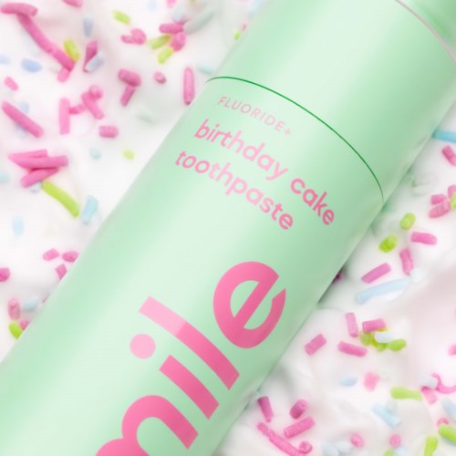 Ein pastellgrüner Tube mit der Aufschrift 'birthday cake toothpaste' umgeben von bunten Streuseln auf einer weißen Oberfläche.