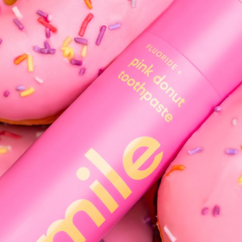 Een roze tube tandpasta met kleurrijke sprinkles op een donut-achtig voorwerp.