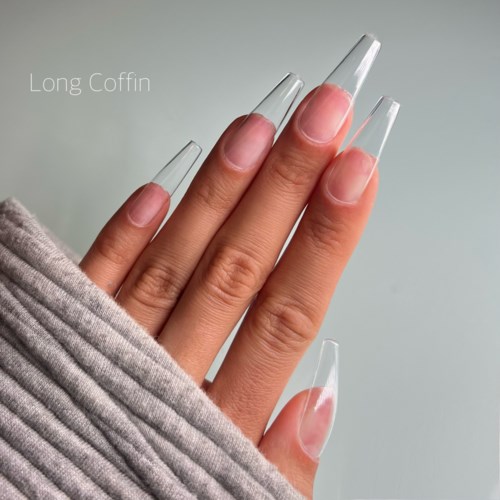 Lange, kistförmige klare Acrylnägel an Fingern, teilweise bedeckt mit hellfarbigem Stoff.