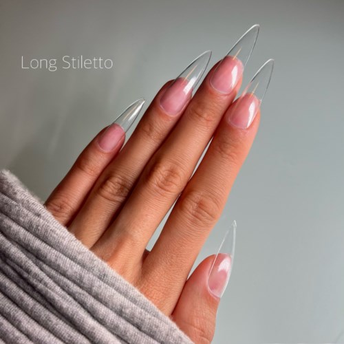Long, clear, natural nails with a glossy finish, shown on a hand partly covered with a gray sleeve.