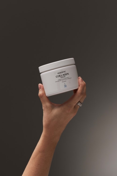 Dłoń trzyma biały słoik z napisem 'Hyaluronic Collagen'. Tło jest ciemne i proste.