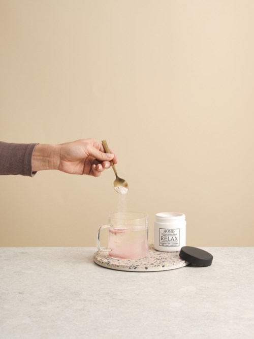 En hand skopar puder från en burk in i ett glas med en sked, med ett lugnande tema och minimal bakgrund.