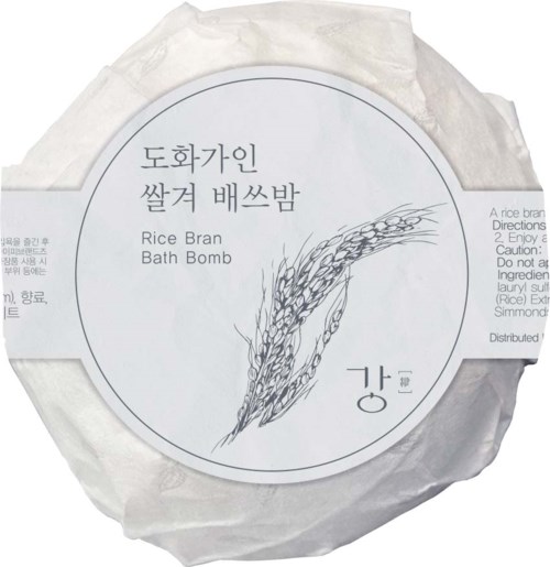 Läpimäinen riisinkirsto kylpypommi, jossa on koreankielistä ja englantilaista tekstiä ja yksinkertainen riisin kuva.