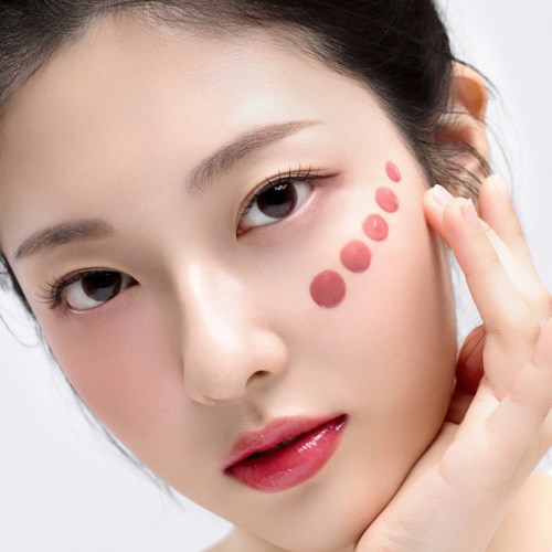 A woman with makeup on her face, with red dots on her cheek, touching her face gently.