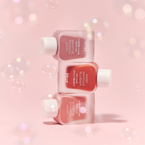 Three pink bottles of moisturizer are stacked, with bubbles and soft light in the background.