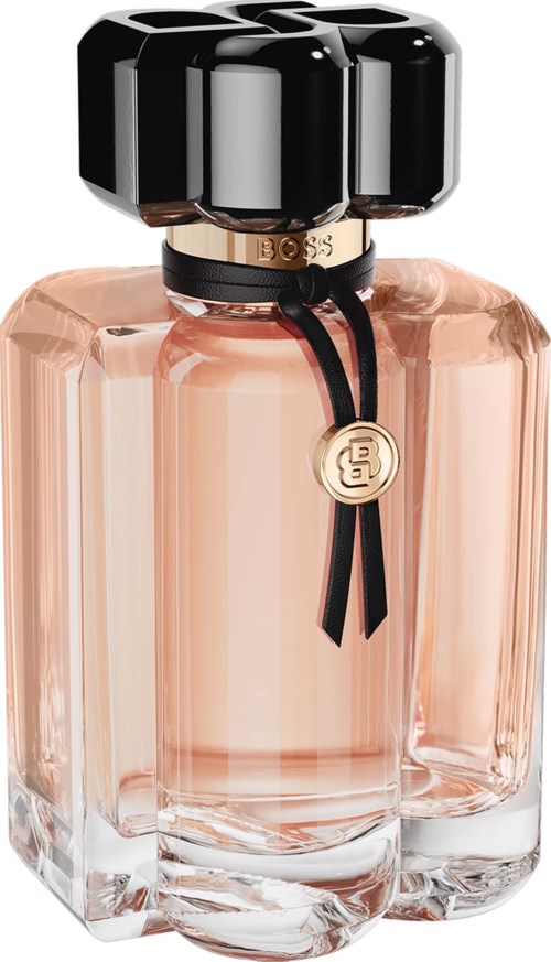 A perfume bottle with a black cap, gold details, and a black ribbon with a gold charm, filled with pink perfume.