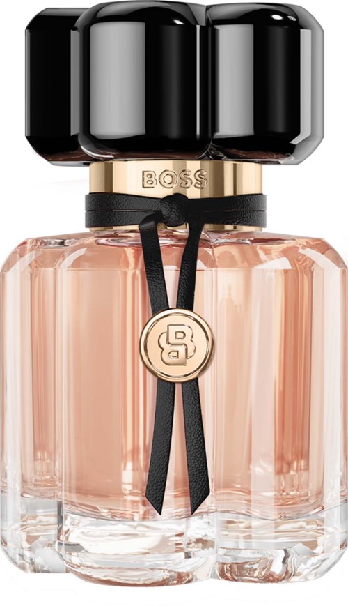 A perfume bottle with a black top, gold band, and a pinkish liquid inside, decorated with a black ribbon and gold medallion.
