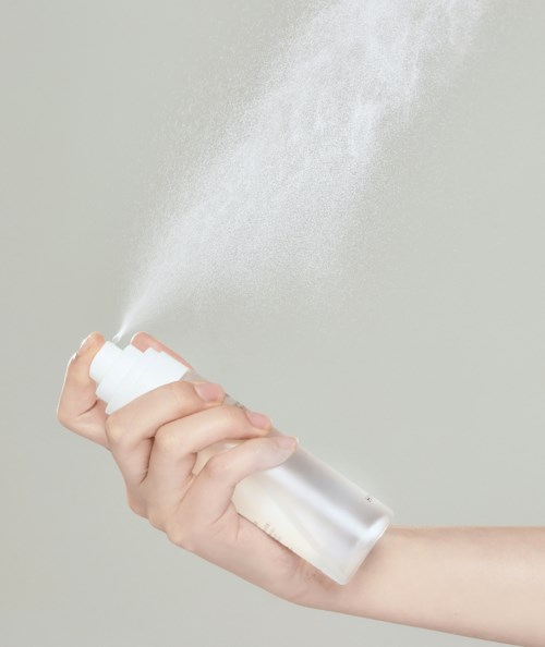 En hand sprayar ett fint moln från en vit sprayburk.