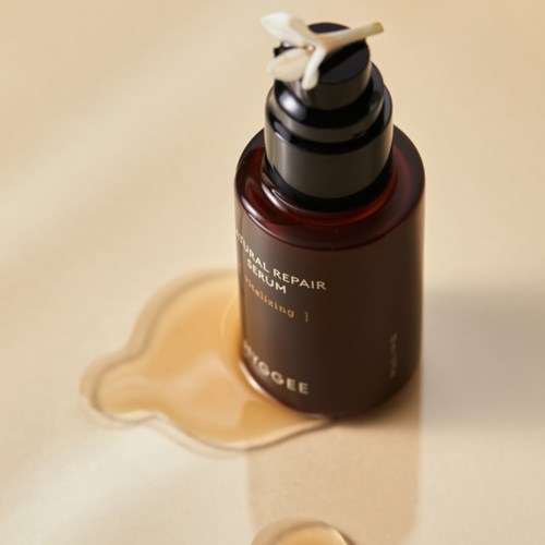 En brun flaska med pump, märkt 'Natural Repair Serum,' ställer på en ljus yta med spilld produkt i närheten.