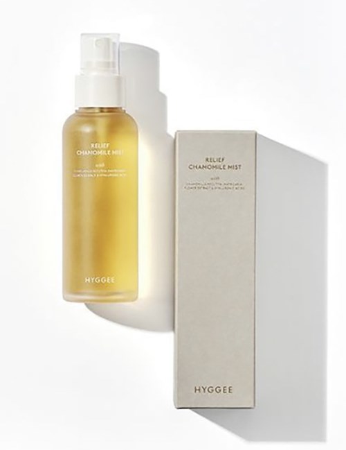 En gul flaska märkta 'Relax Chamomile Mist' bredvid en vit låda med samma märkning inuti. Skuggor kastas på vit bakgrund.