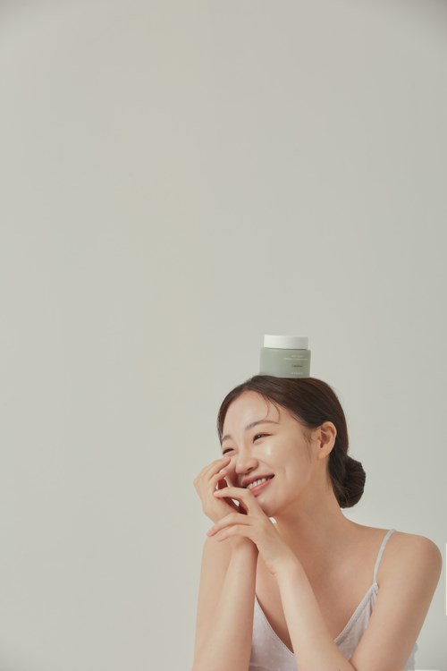 Een vrouw lacht met een kleine container op haar hoofd, gekleed in een witte top, in een eenvoudige studio.