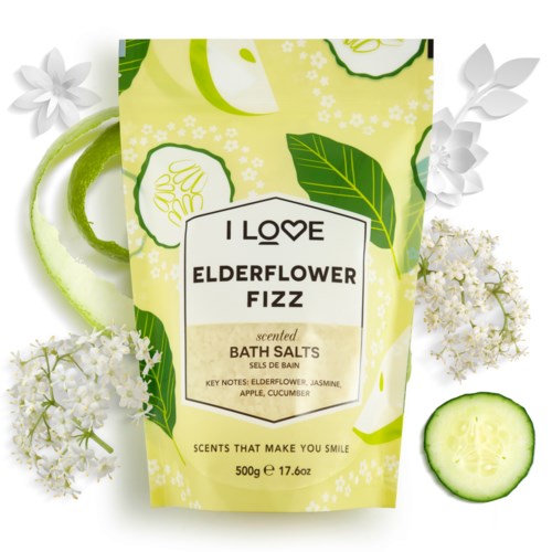 Ett ljust grönt och vitt badsaltspaket med fläderblom, jasmin, äpple och gurka-doft, omgiven av färska växter.