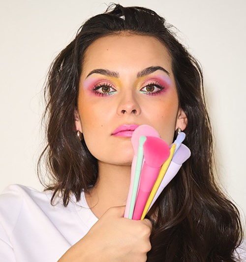 Eine Frau mit buntem Augen-Make-up hält pastellfarbene Make-up-Pinsel in der Nähe ihres Gesichts.