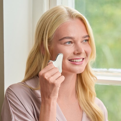 A woman with blonde hair smiling and talking on a white cordless phone near a window.