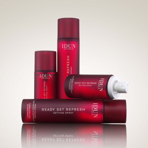 Four red cans and one white tube of IDUN Minerals Ready Set Refresh setting spray are arranged neatly.