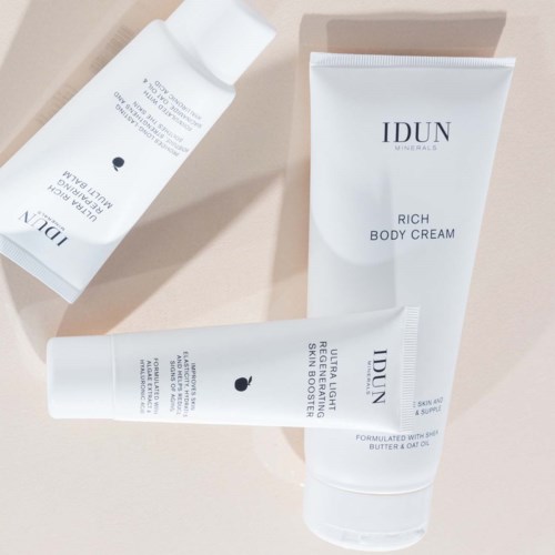 Three white tubes of skincare product on a light surface, labeled as IDUN Minerals, Rich Body Cream, and Brightening Serum.