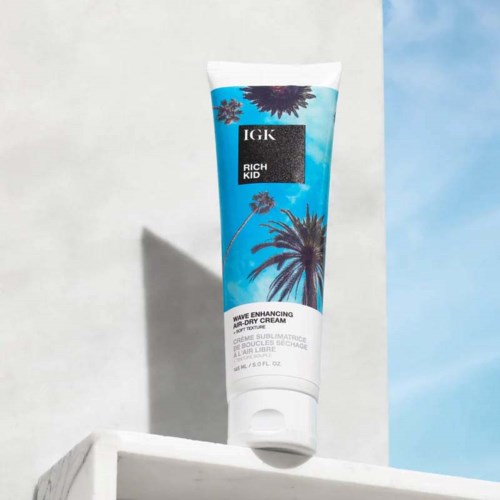 En tube af IGK Rich Kid Wave Enhancing Air-Dry Cream på en hvid kant mod en lys baggrund.
