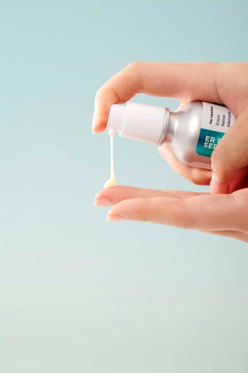 En hand håller i en liten flaska som sprutar ut kräm eller gel i den andra handen. Ljus bakgrund med mjuka färger.