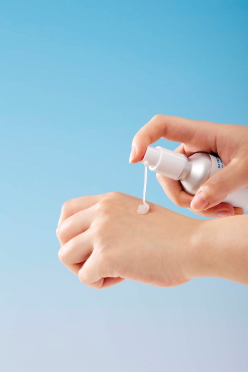 En person applicerar en rosaaktig kräm eller lotion på sin hand från en sprayflaska.