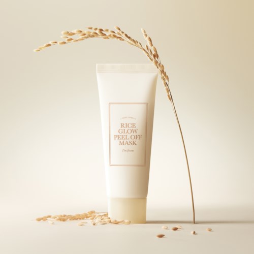 En hvit tube med rice glow peel-off maske med riskorn rundt den og en tørket plante som lener seg mot den.