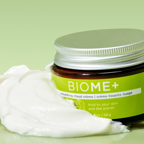 En krukke med hudkrem merket 'BIOME+', med litt krem spredt ved siden av på en lys grønn bakgrunn.