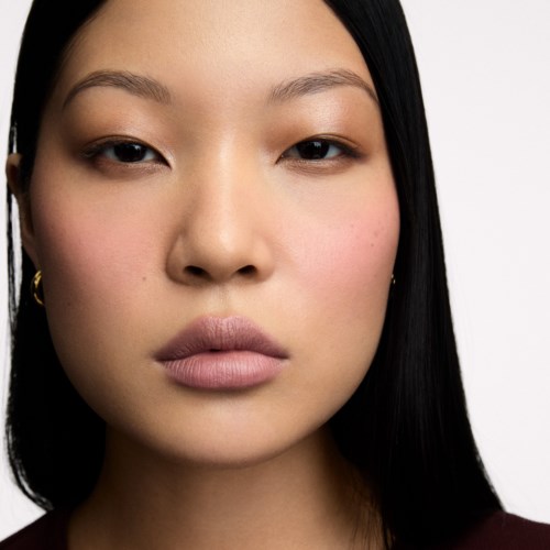 Close-up of a woman with smooth skin, dark hair, and neutral expression, facing the camera directly.