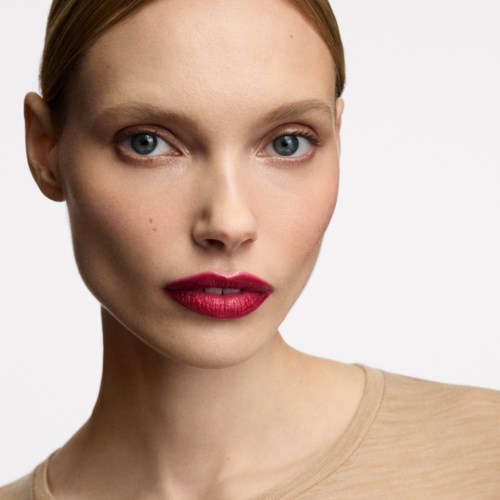 A young woman with red lipstick and blue eyes, looking directly at the camera, wearing a beige top.