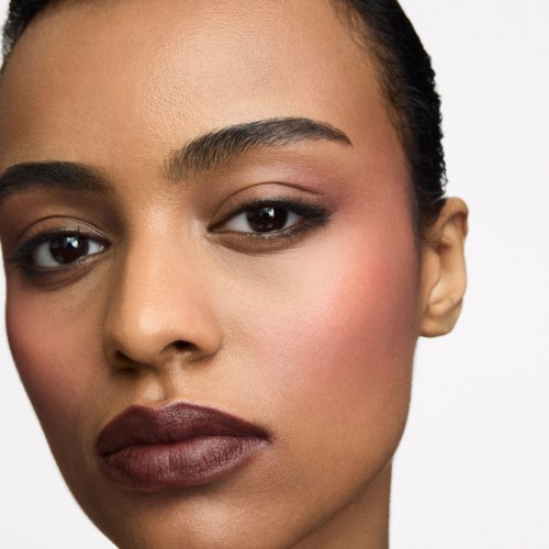 Close-up of a woman with flawless skin, dark hair, and neutral makeup, looking at the camera.