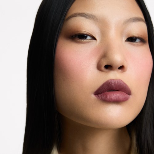 Close-up of a woman with long black hair, lightly closed eyes, and matte lipstick.