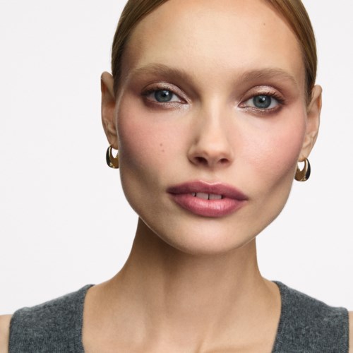 A woman with fair skin, red hair, blue eyes, gold hoop earrings, and a neutral expression.