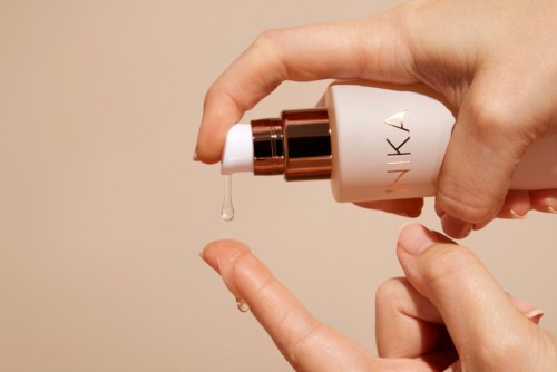 En hand håller en pumpflaska som släpper ut en liten mängd crème eller serum på ett finger.