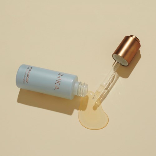 A blue skincare bottle with a dropper cap, some liquid spilled on a beige surface.