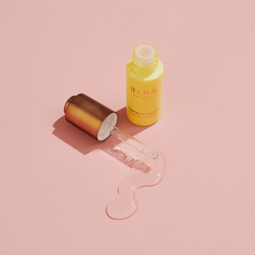 A yellow bottle with a dropper cap releasing a clear liquid onto a pink surface.