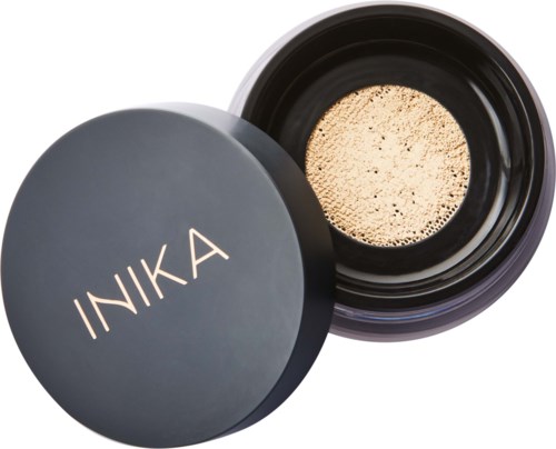 Ein schwarzer Behälter mit dem Namen INIKA auf dem Deckel, geöffnet, um beige Pulver zu zeigen.