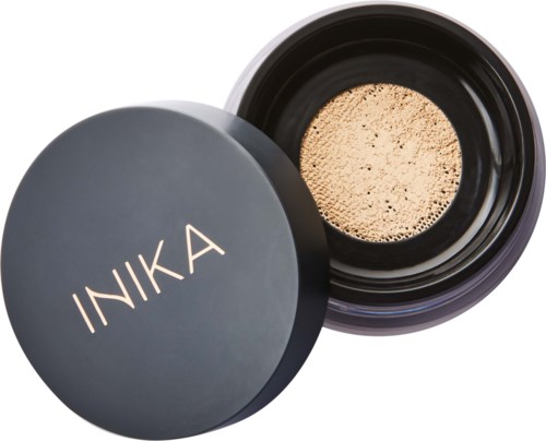 Schwarzer Behälter mit beige Pulver, beschriftet INIKA. Es sieht aus wie ein Make-up- oder Kosmetikprodukt.
