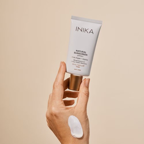 Eine Hand hält eine Tube mit INIKA natürlicher Sonnencreme mit einem Klecks Creme auf der Haut.