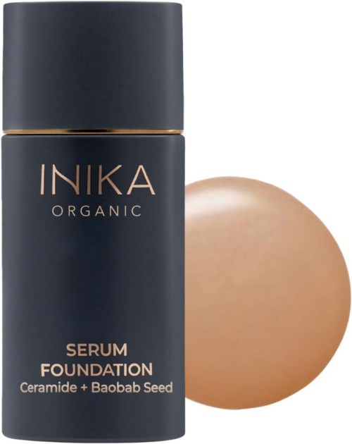 A dark bottle labeled INIKA Organic Serum Foundation with ceramic and Baobab seed, next to a beige round object.