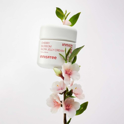 Een potje Innisfree Cherry Blossom Glow Jelly Cream omringd door roze kersenbloesems en groene bladeren.