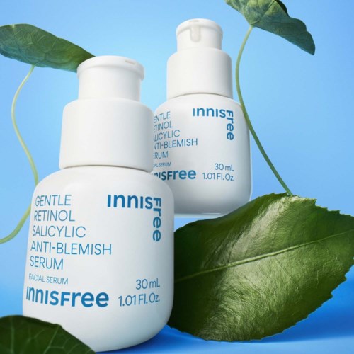 Twee witte flessen van Innisfree huidverzorgingsserum tussen groene bladeren op een blauwe achtergrond.