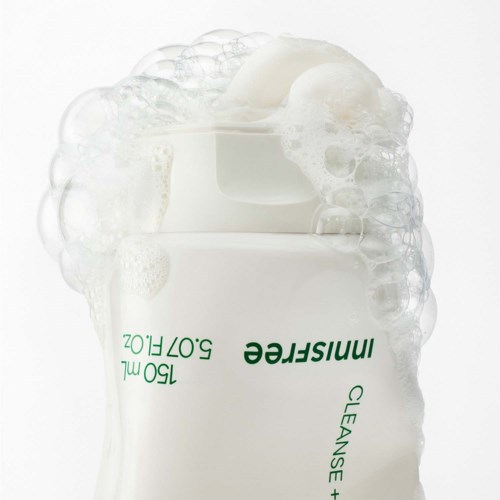 Een witte pot met groene tekst met een huidverzorgingsproduct, bedekt met schuim en bellen.