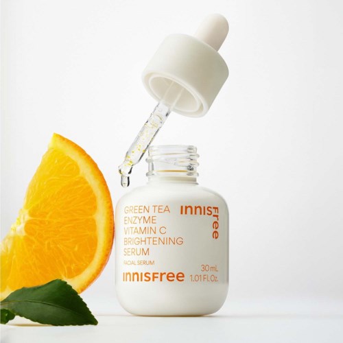 Een witte fles Innisfree gezichtsserum met pipet, sinaasappelschijf en groen blad ernaast.