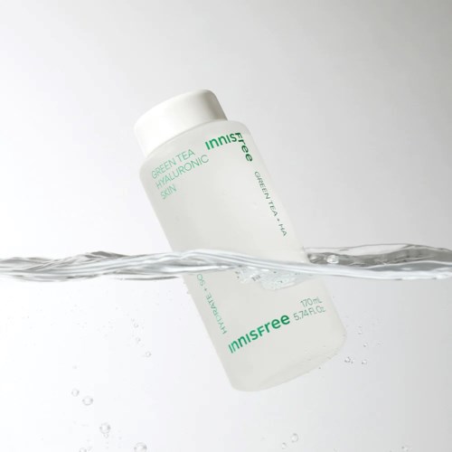 A white bottle partially submerged in water, labeled 'Innisfree Green Tea Hyaluronic'.