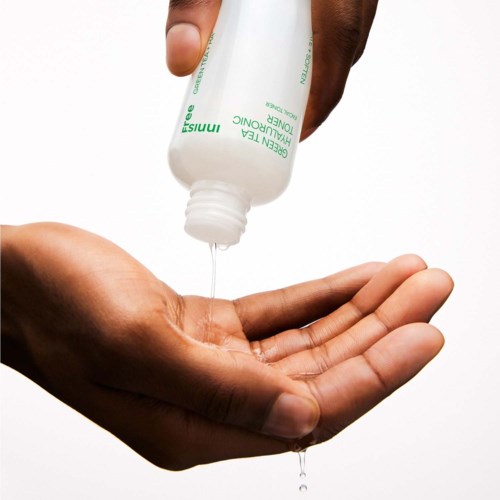 Een hand houdt een fles groene thee reinigingsvloeistof en giet een beetje in de andere hand.