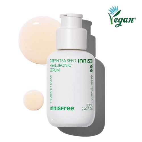En vit hudvårdsflaska märkt 'Innisfree Green Tea Seed Hyaluronic Serum' med två krämliknande droppar i närheten.