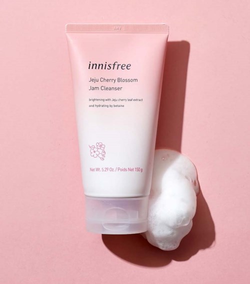 Rosaröd tub med Innisfree Jeju Cherry Blossom Jam Cleanser och skum på rosa bakgrund.