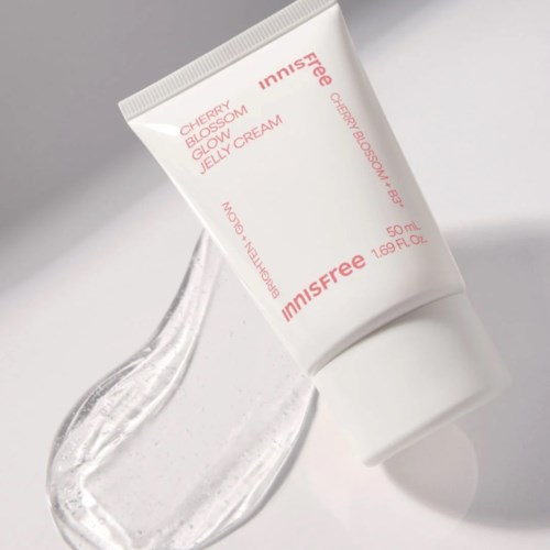 Eine weiße Tube mit Jeju Blossom Jelly Cream mit pinkem und orangefarbenem Text liegt auf einer weißen Oberfläche.