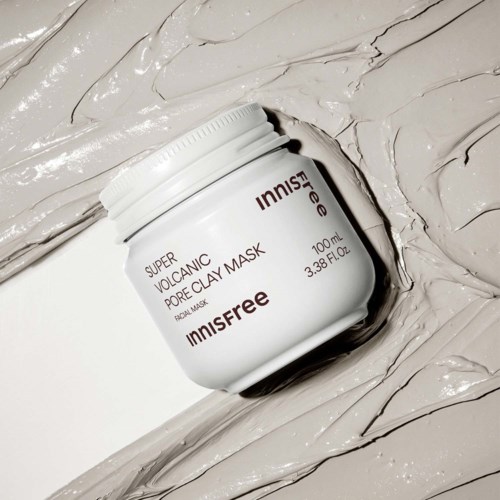Een witte pot met INNISFREE Super Volcanic Pore Clay Mask op een romige ondergrond.
