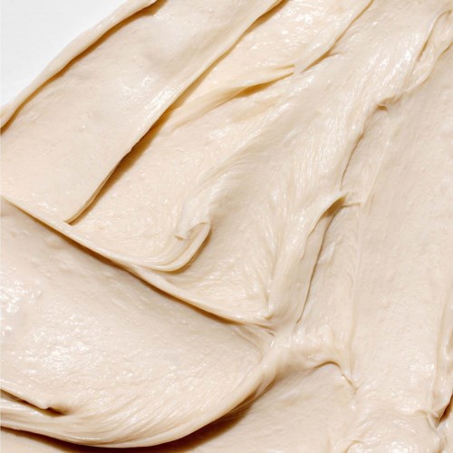 Romige, beige kleurige huidverzorgingsproduct uitgespreid in een spiraalachtig patroon.