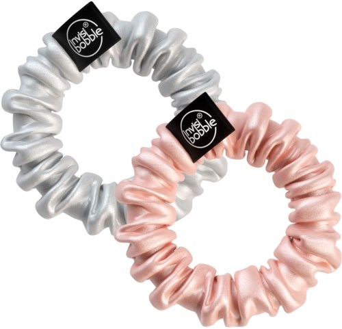 Two satin scrunchies, one in silver and one in pink, with black labels, are intertwined.