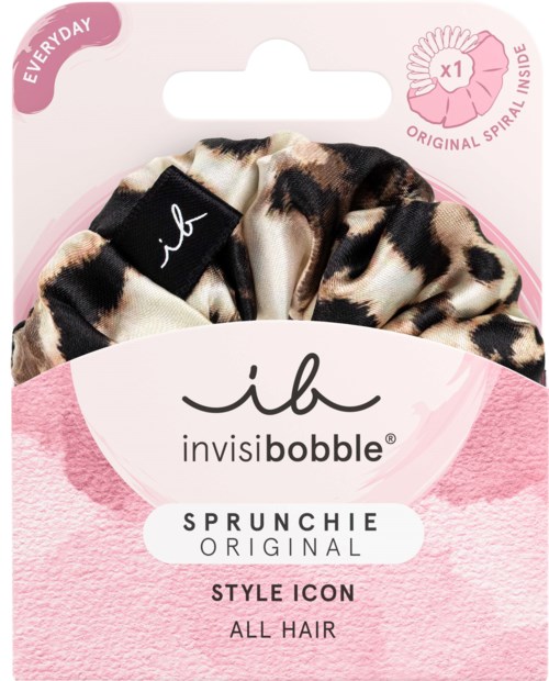 A leopard print hair scrunchie with a black tag, packaged in pink wrapping with brand and product details.